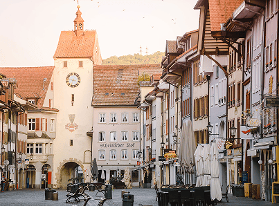 Historische Stadtstraße mit Fachwerkhäusern und einem markanten Uhrturm im Hintergrund. Ruhe und Tageslicht.