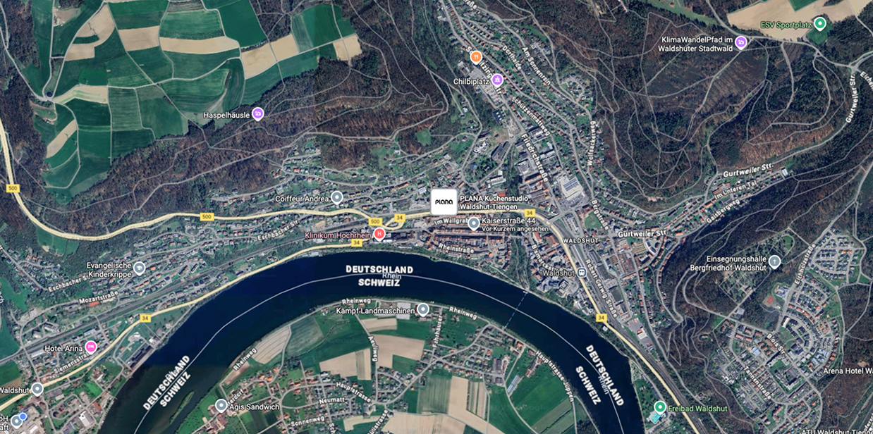 Eine Satellitenansicht einer Stadt an einem Fluss mit umliegenden Feldern und Wäldern. Ortsanmerkungen sind sichtbar.