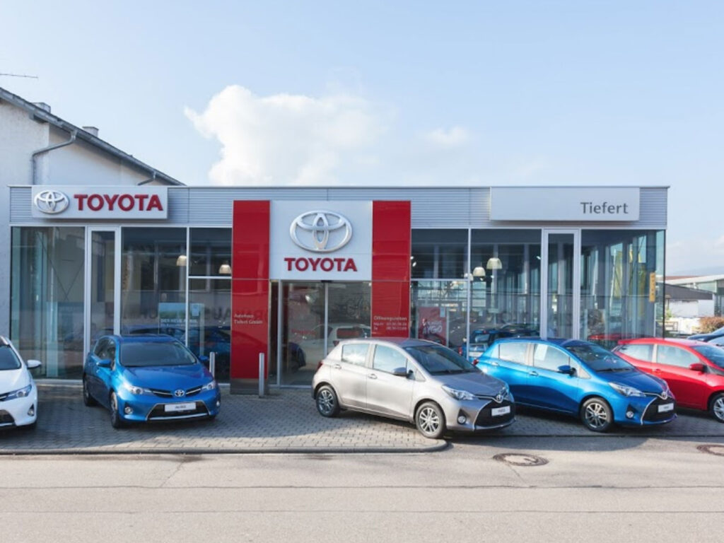 Toyota Autohaus mit verschiedenen Fahrzeugen in einer Auslage. Klarer Himmel und moderne Architektur.