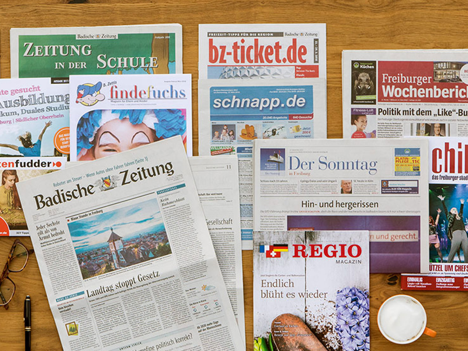 Eine Sammlung von Zeitungen und Magazinen auf einem Tisch, darunter regionale Nachrichten und Schulzeitschriften.