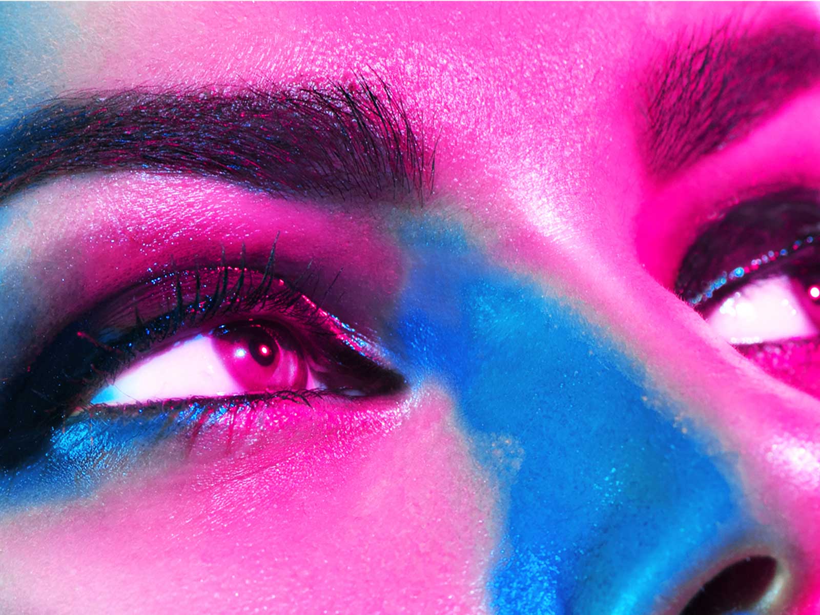 Nahaufnahme eines Augenpaares mit bunten, intensiven Lichtern in Pink und Blau, die die Gesichtszüge betonen.