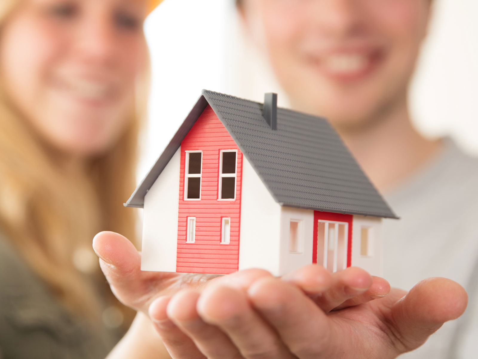 Ein Paar hält ein Modellhaus in der Hand, lächelnd, mit Fokus auf das Haus.