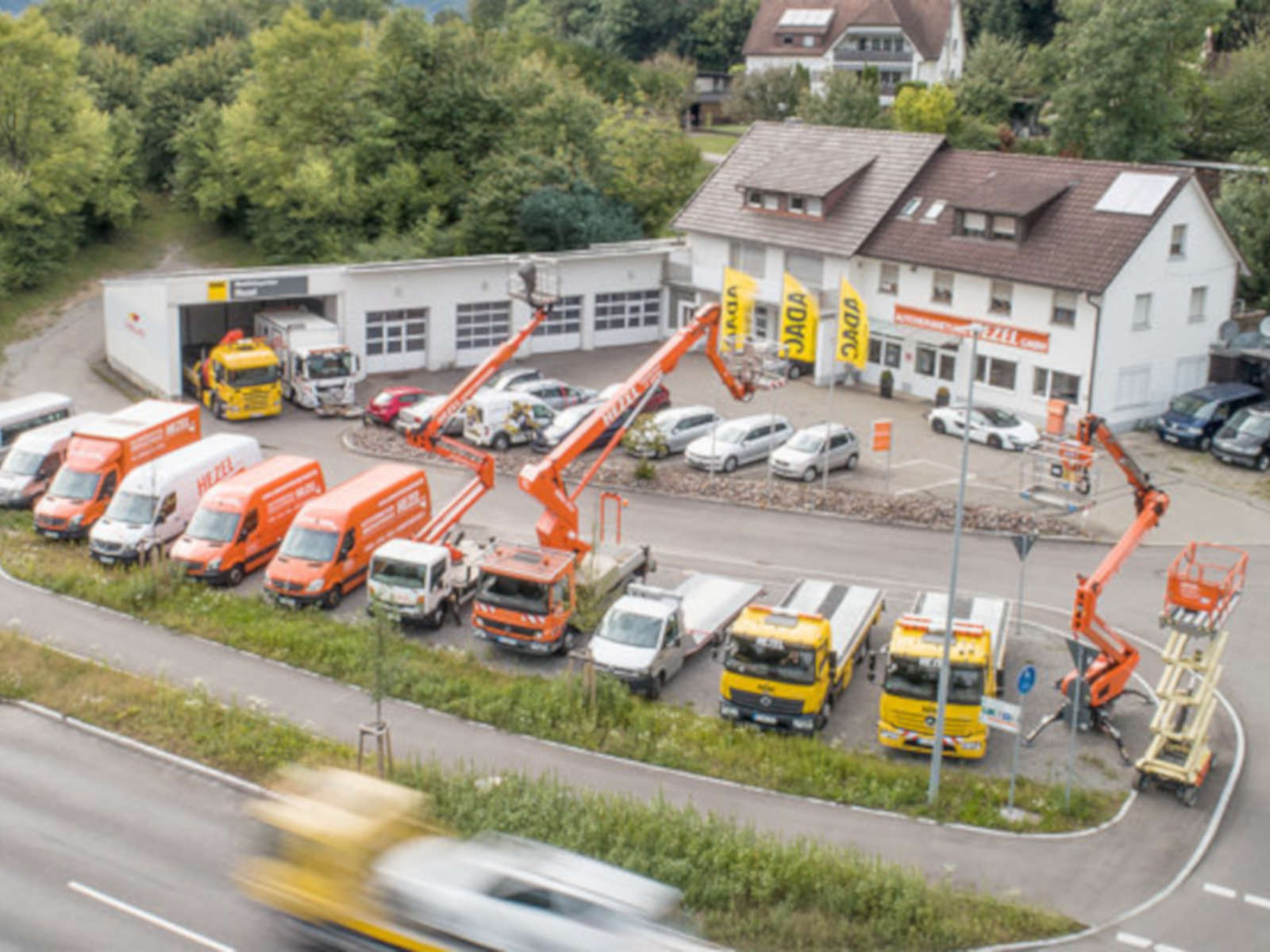 Luftaufnahme eines Unternehmens mit verschiedenen Fahrzeugen und Arbeitsbühnen auf einem Parkplatz vor einem Gebäude.