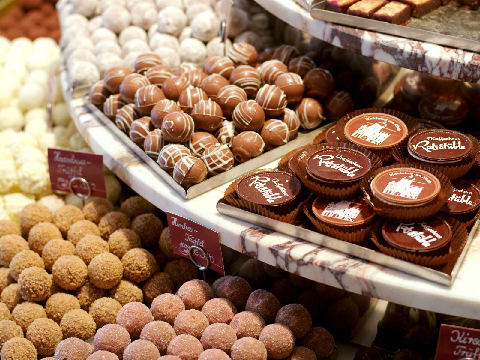 Eine Auswahl an Pralinen und Trüffeln in einer Konditorei, dekorativ auf einem Regal präsentiert.