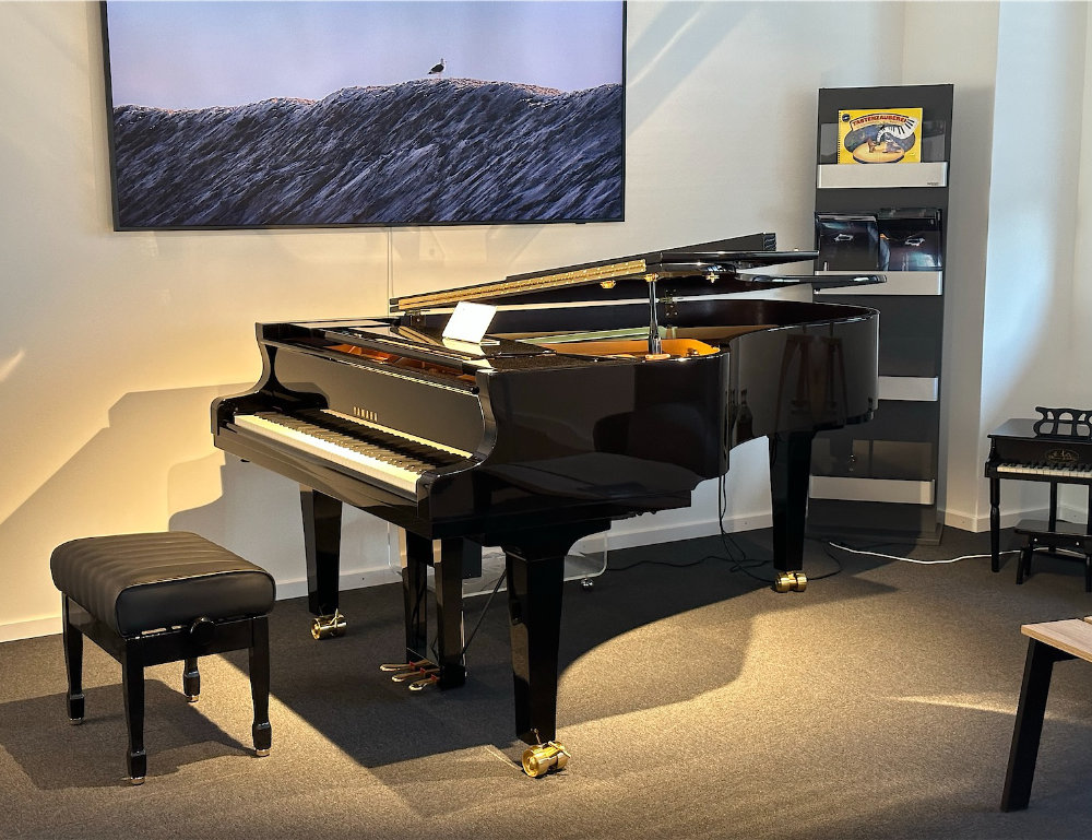 Ein schwarzes Flügelpiano steht in einem Raum, daneben ein Hocker und ein Regal mit Musikmaterial.