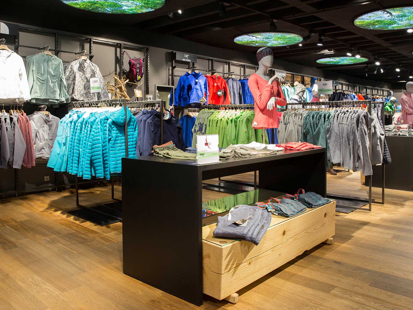 Ein Innenansicht eines Sportbekleidungsgeschäfts mit verschiedenen Jacken und Kleidung, präsentiert auf Kleiderständern.