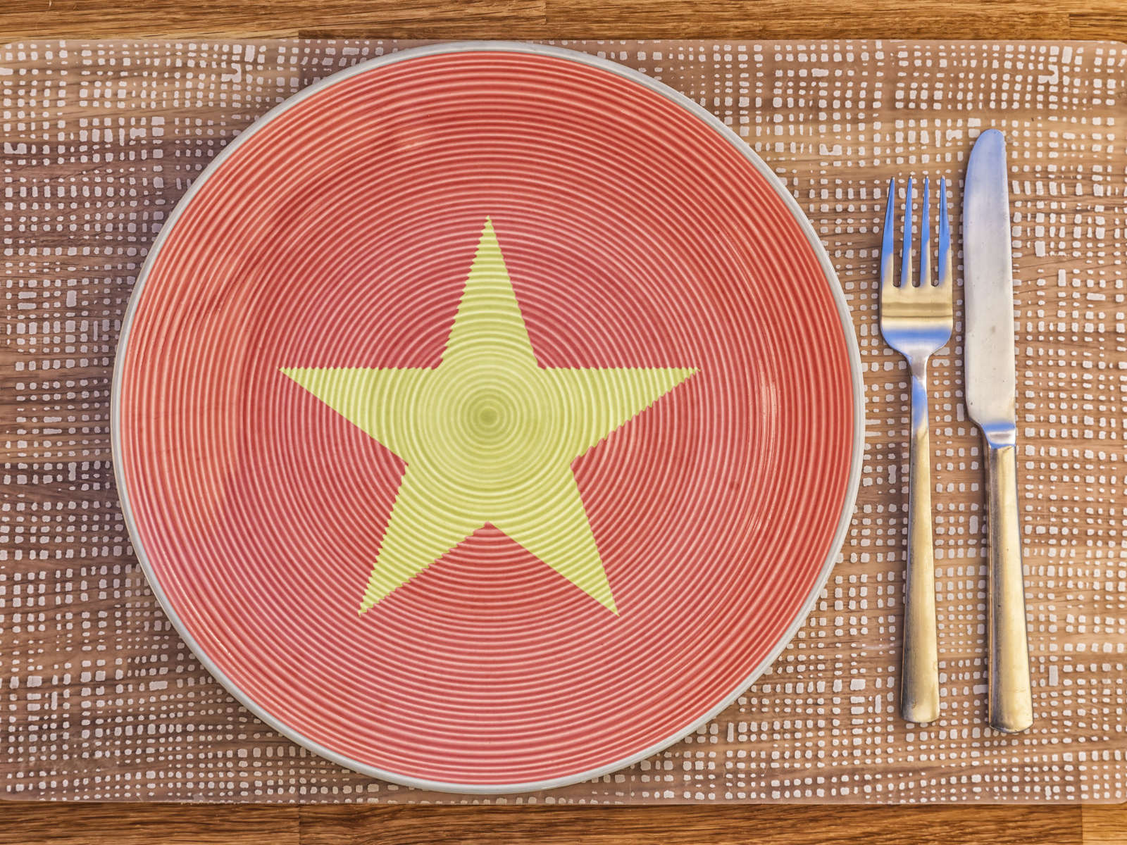 Ein dekorativer Teller mit rot-gestreiftem Muster und einem gelben Stern, daneben Besteck auf einem Platzdeckchen.