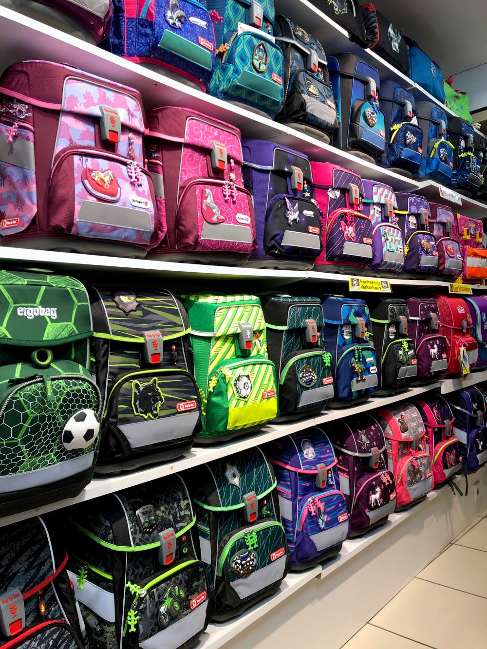 Eine Wand mit verschiedenen bunten Schulranzen, sortiert nach Designs und Farben.