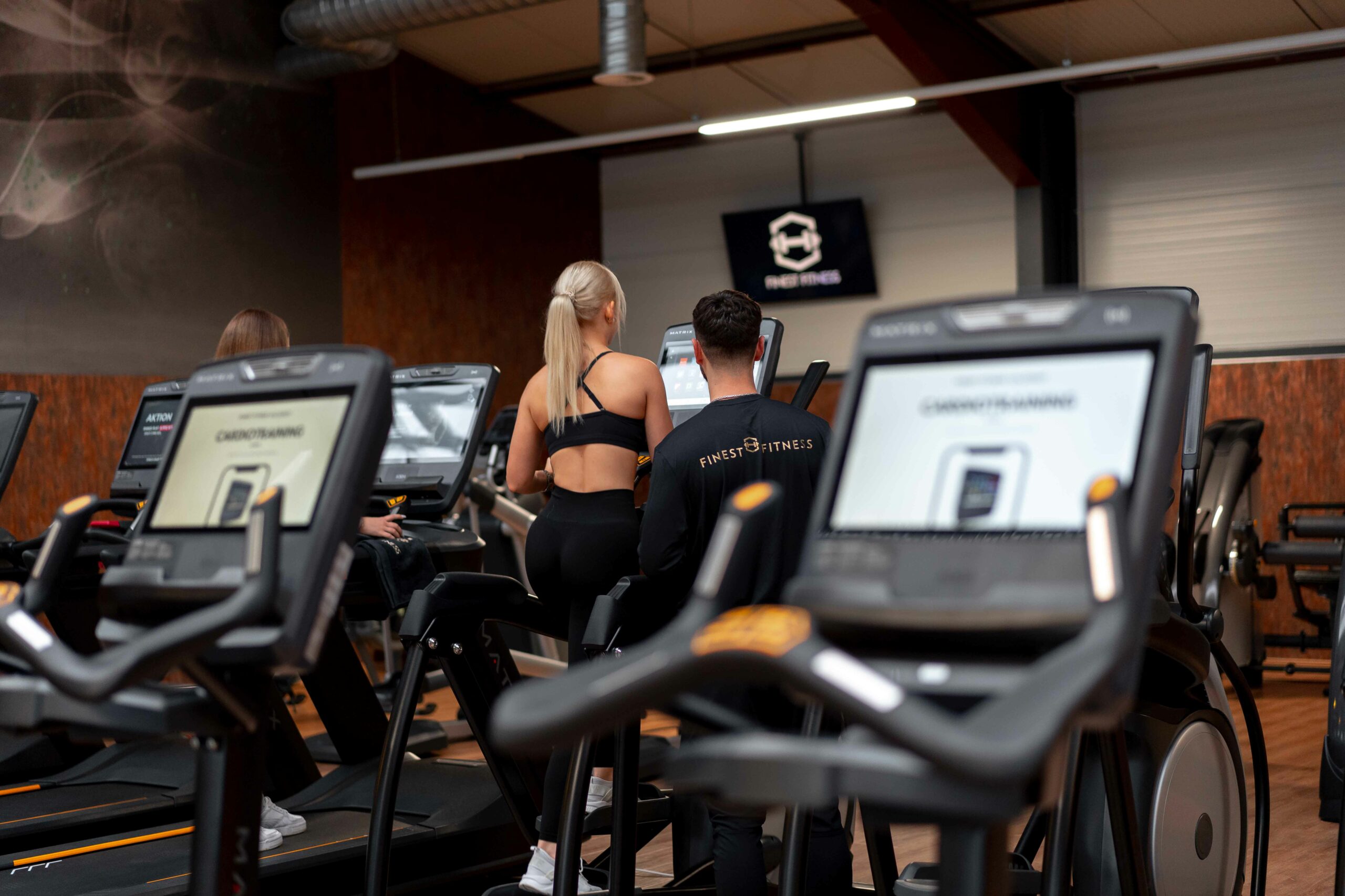Zwei Personen trainieren an Crosstrainern in einem modernen Fitnessstudio.