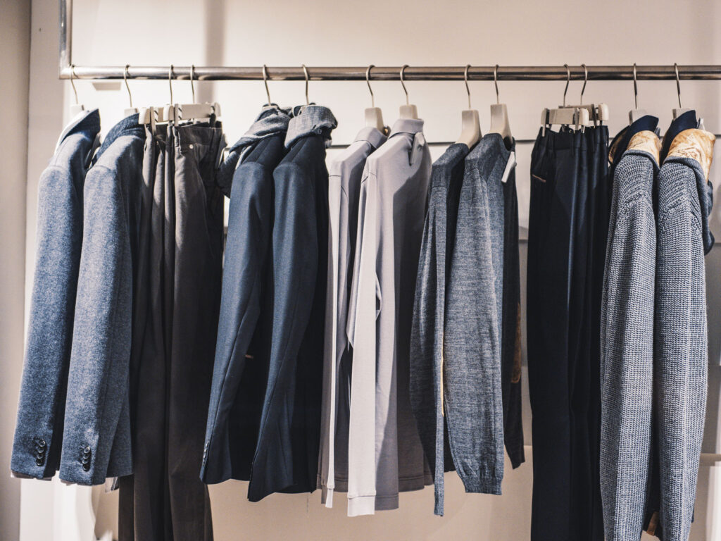 Kleidung auf einem Kleidungsständer, darunter Jacken, Hemden und Hosen in verschiedenen Blautönen und Grau.