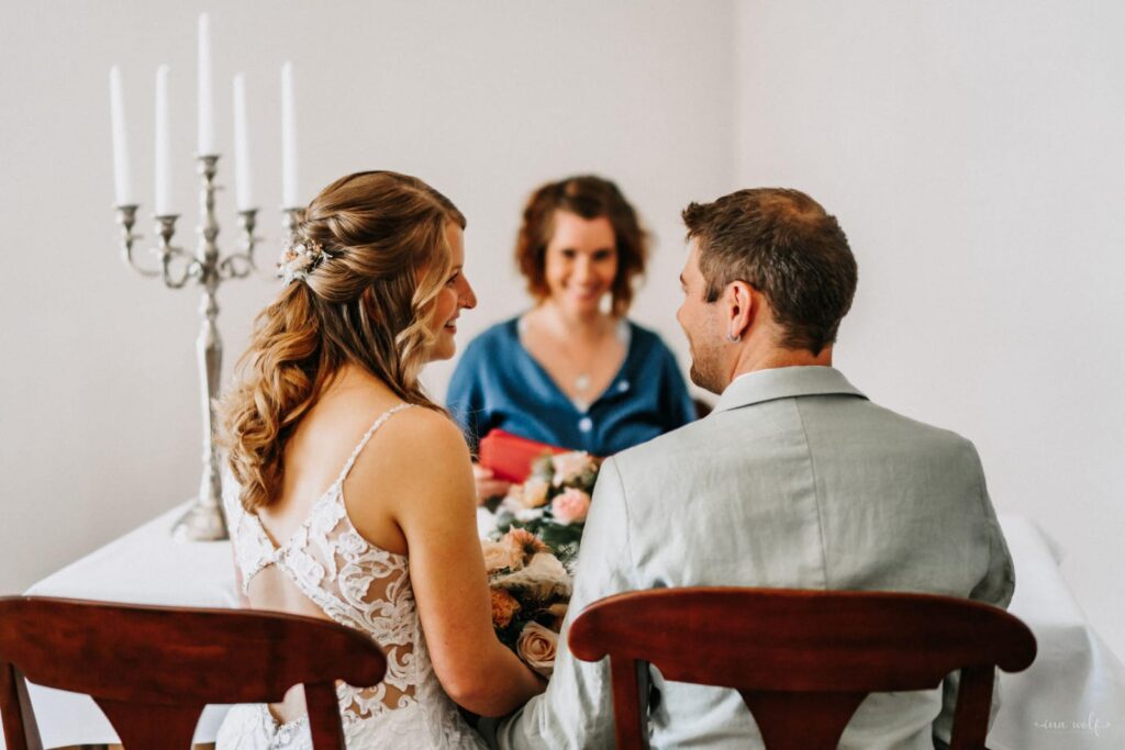 Hochzeitszeremonie mit einem Paar, das sich an einem Tisch gegen einen Druck von Blumen und Kerzen unterhält.