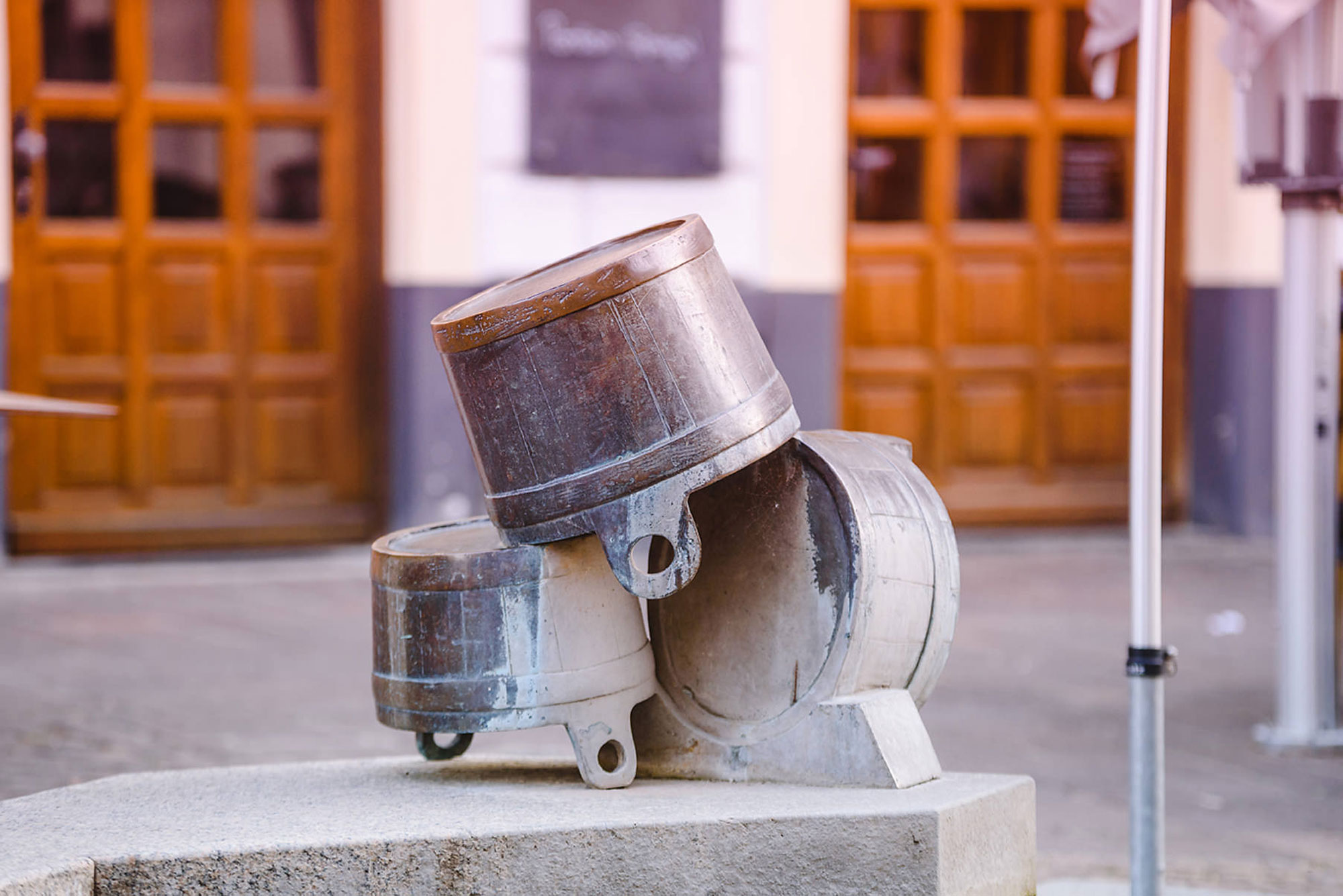 Drei übereinander gestapelte metallene Behälter stehen auf einem Sockel in einer urbanen Umgebung.