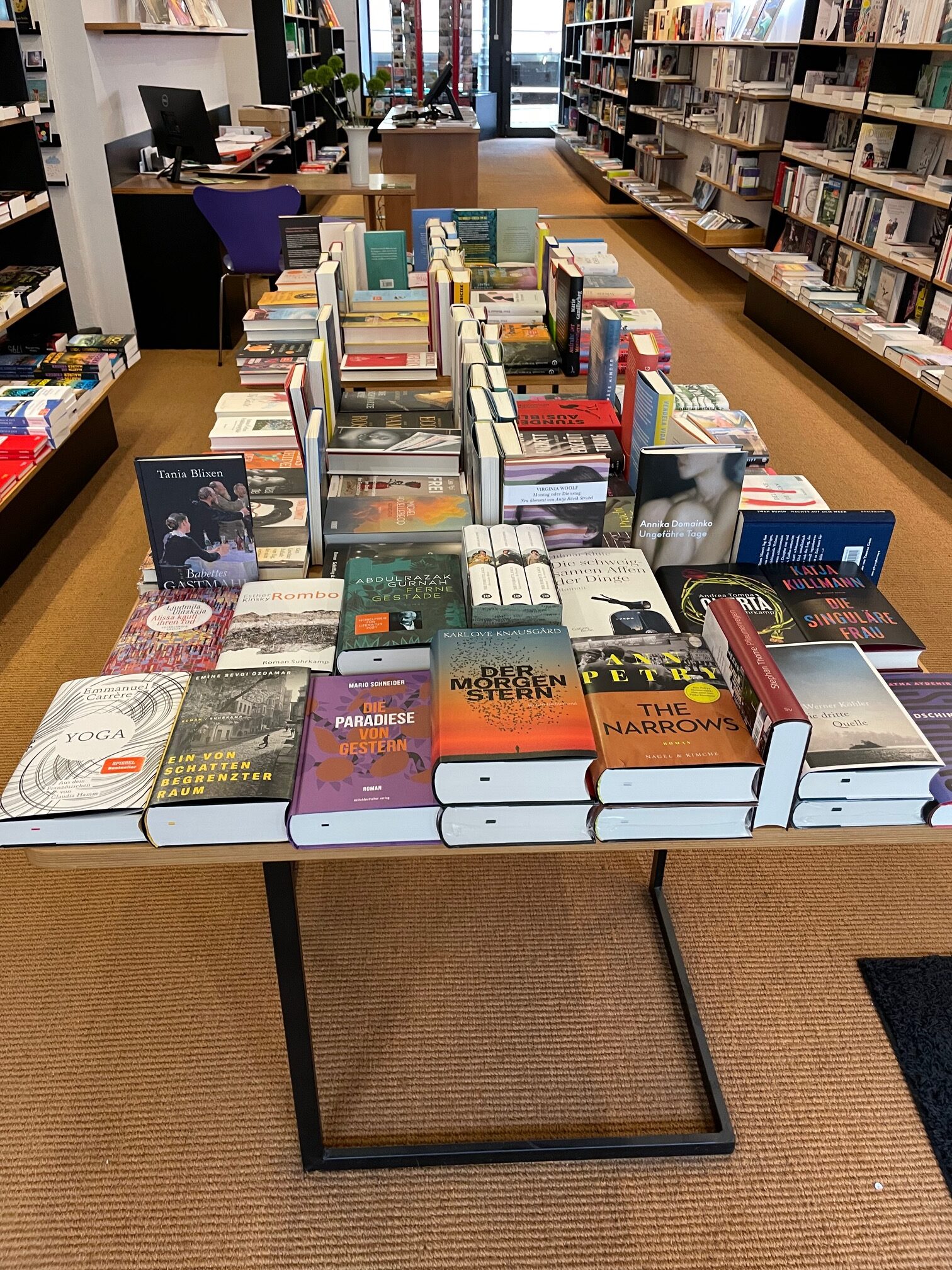 Ein Tisch mit einer Vielzahl von Büchern in einem Buchladen, umgeben von Regalen mit weiteren Büchern.