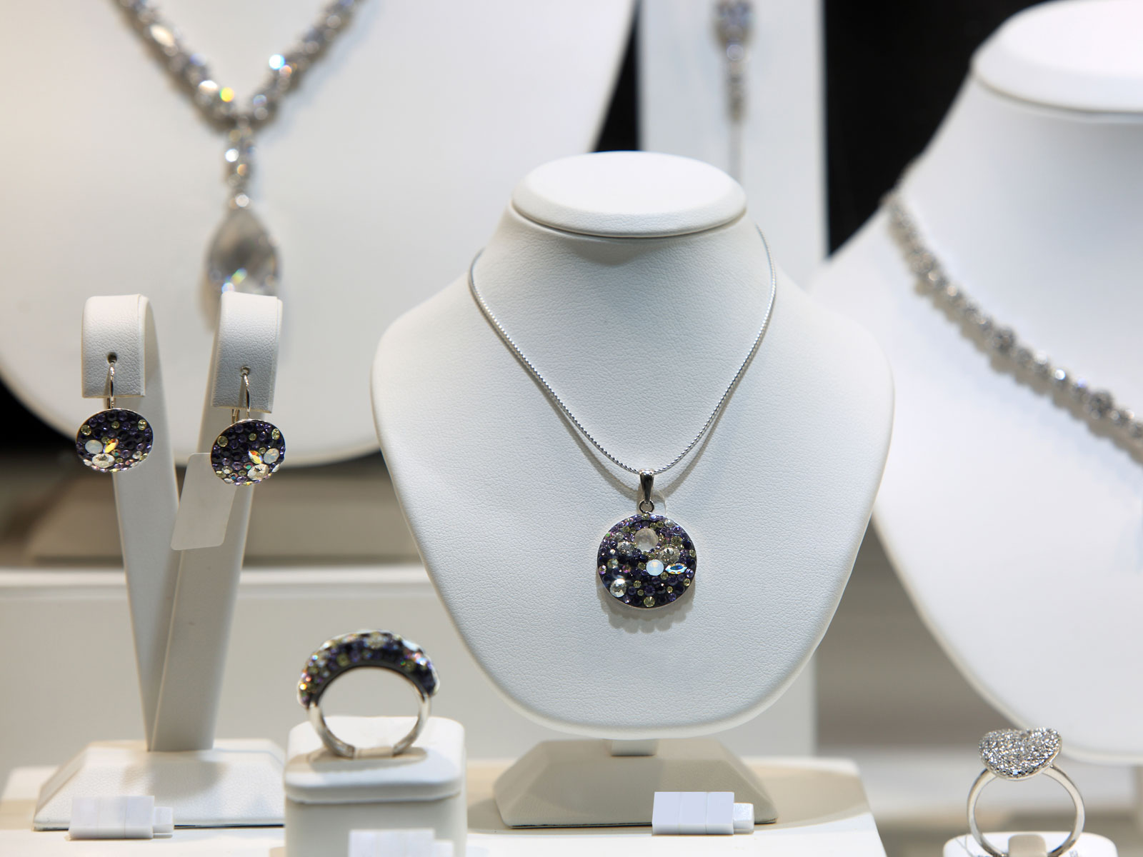 Schmuckvitrine mit Ohrringen, einem Anhänger, einer Kette und Ringen, alle glitzernd mit bunten Steinen.