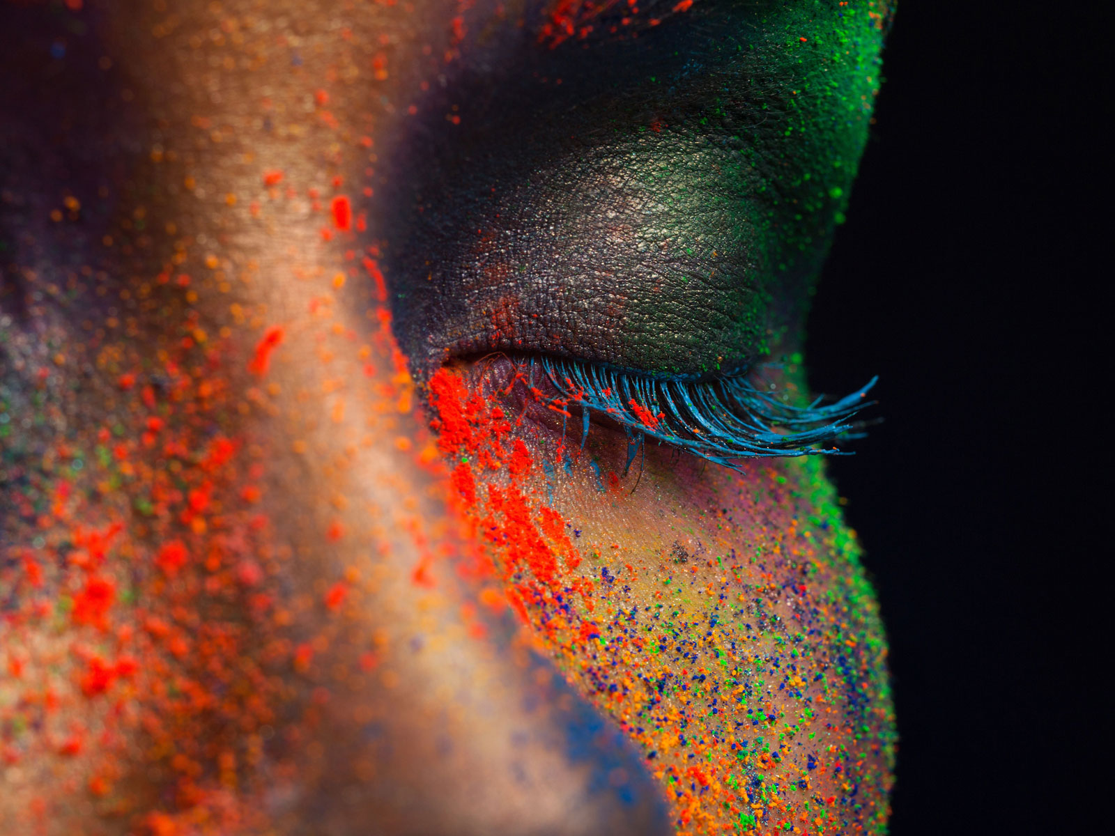 Nahaufnahme eines geschlossenen Auges, umgeben von buntem, glitzerndem Puder in Neonfarben.