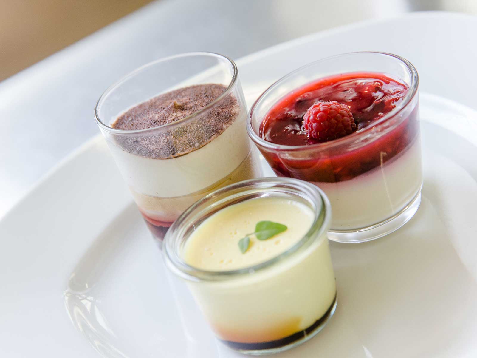 Drei Dessertgläser mit unterschiedlich gefüllten Cremes: Schokoladenmousse, Himbeersauce und Vanillecreme.