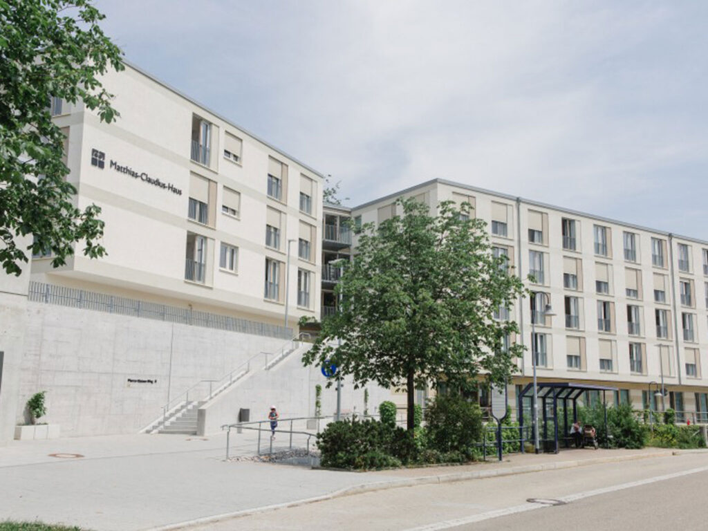 Modernes Gebäude mit dem Schriftzug „Matthias-Claudius-Haus“ und Grünflächen im Vordergrund.