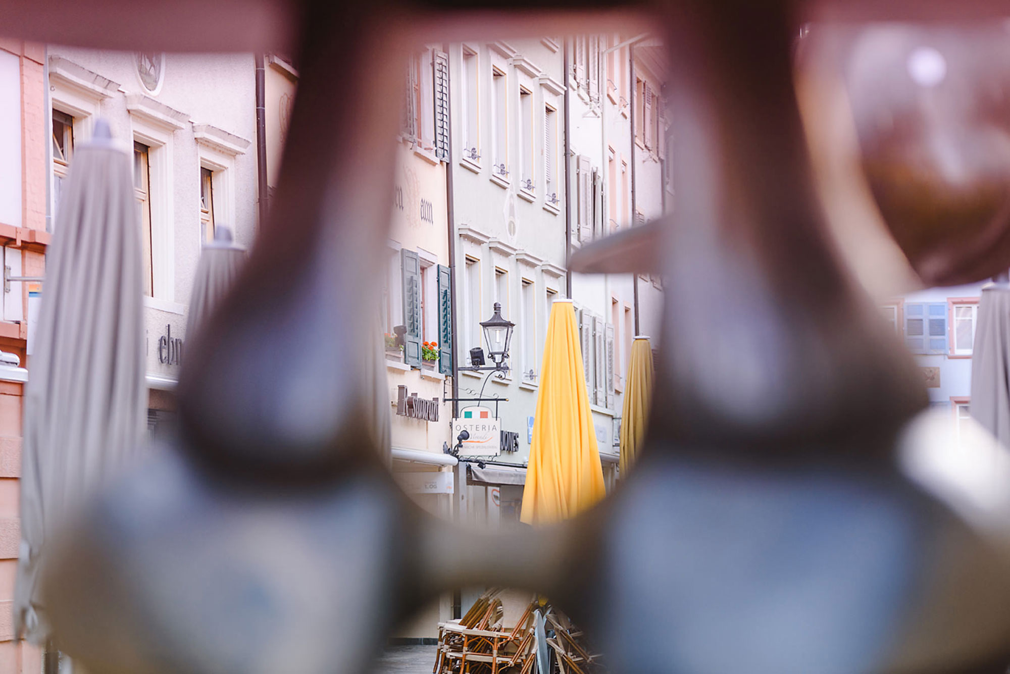 Sicht durch eine enge Öffnung auf eine Straße mit bunten Restaurantmarkisen und dekorativen Häuserfronten.