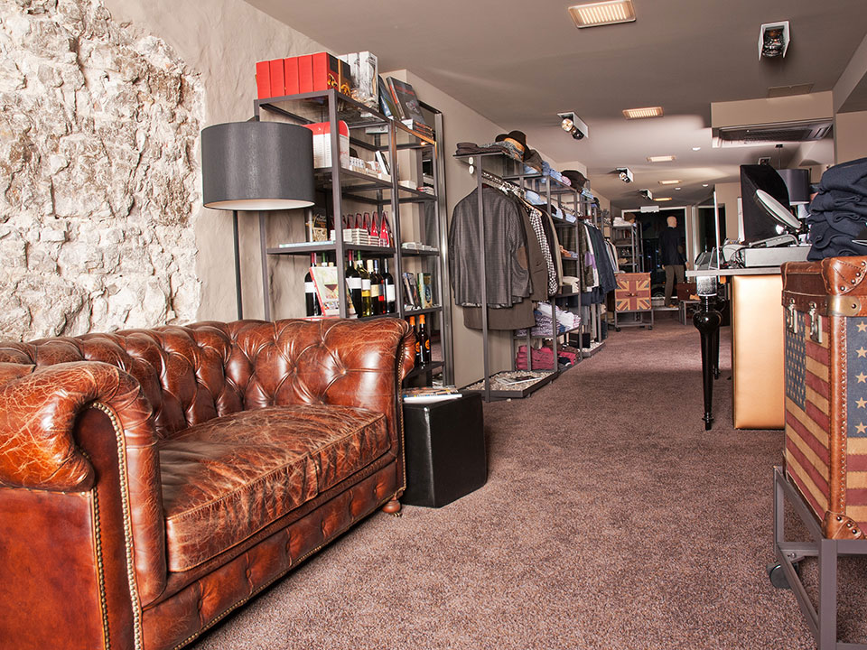 Ein stilvoller Raum mit einer Ledercouch, Regalen voller Kleidung und Accessoires sowie einem dekorativen Koffer.